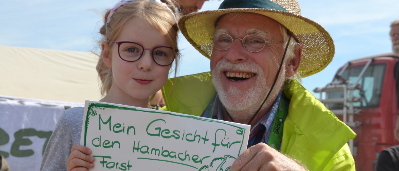 Enkelin und Großvater zeigen Schild "Mein Gesicht für den Hambi"