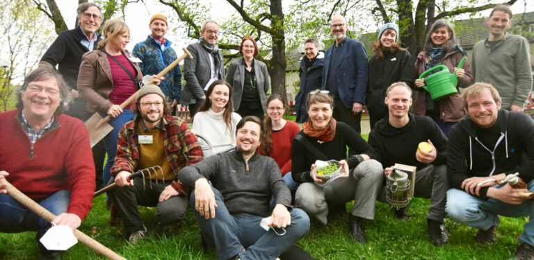 Gruppenfoto vom Plattform Team mit Gästen, einige Personen haben landwirtschaftliche Utensilien in der Hand