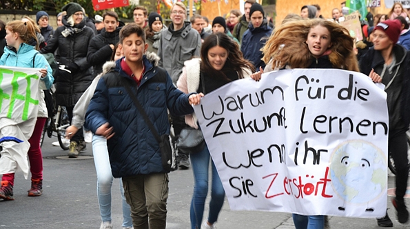 Junge Schüler.innen rennen mt einem Plakat auf der Demo auf dem Steht: Warum für die Zukunft lernen wenn ihr sie zerstört?