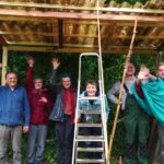 7 Personen freuen sich, dass das Tomatenhaus fertig ist und dass sie im Trockenen Stehen können