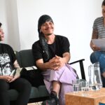 3 Personen sitzen auf einer Bank, eine hat ein Kopftuch an.