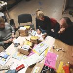 Menschen sitzen um einen Tisch und kleben bunte Karten für das Pop Up Atelier zusammen