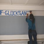 Daniela Baum klebt mit Tape den SChriftzug B4F Glücksanzeiger auf die Wand