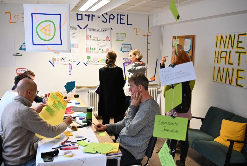Teilnehmende am Bonn4Future Spiel an Arbeitstischen und stehen im Gespräch