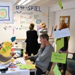Teilnehmende am Bonn4Future Spiel an Arbeitstischen und stehen im Gespräch