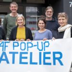 Besucher:innen des B4F PopUpAtelier stehen vor dem Pavillon und halten ein großes Banner auf dem B4F-Pop-UP-Atelier steht