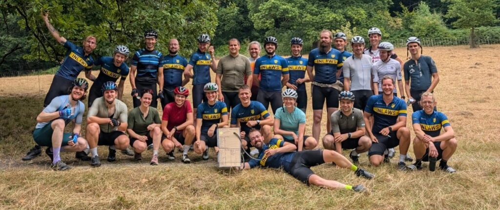 viele junge Menschen in Fahrradkluft strahlen in die Kamera. Sie stehen in und liegen in 2 Reihen im Sonnenschein