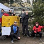 6 Personen mit Weihnachtsbäumen stehen um den gelben Bolle-Bonn Anhänger