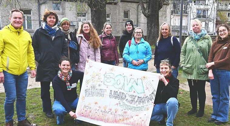 Gesa Maschkowski und Philippa Koska halten das Banner von Bonn blüht und summt. Die Teilnehmenden des Netzwerktreffen Essbares und blühendes Bonn lächeln fröhlich in die Kamera