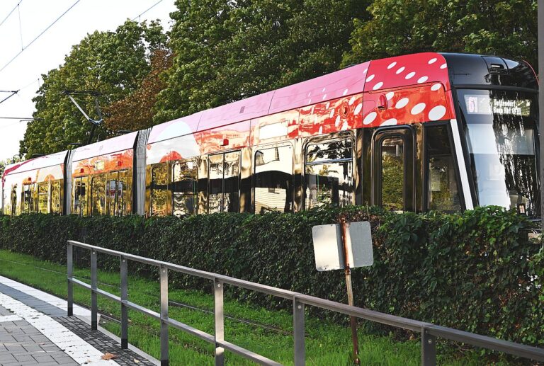 Rote Straßenbahn mit weißen Punkten an der Endhaltestelle mit grüner Hecke und Bäumen
